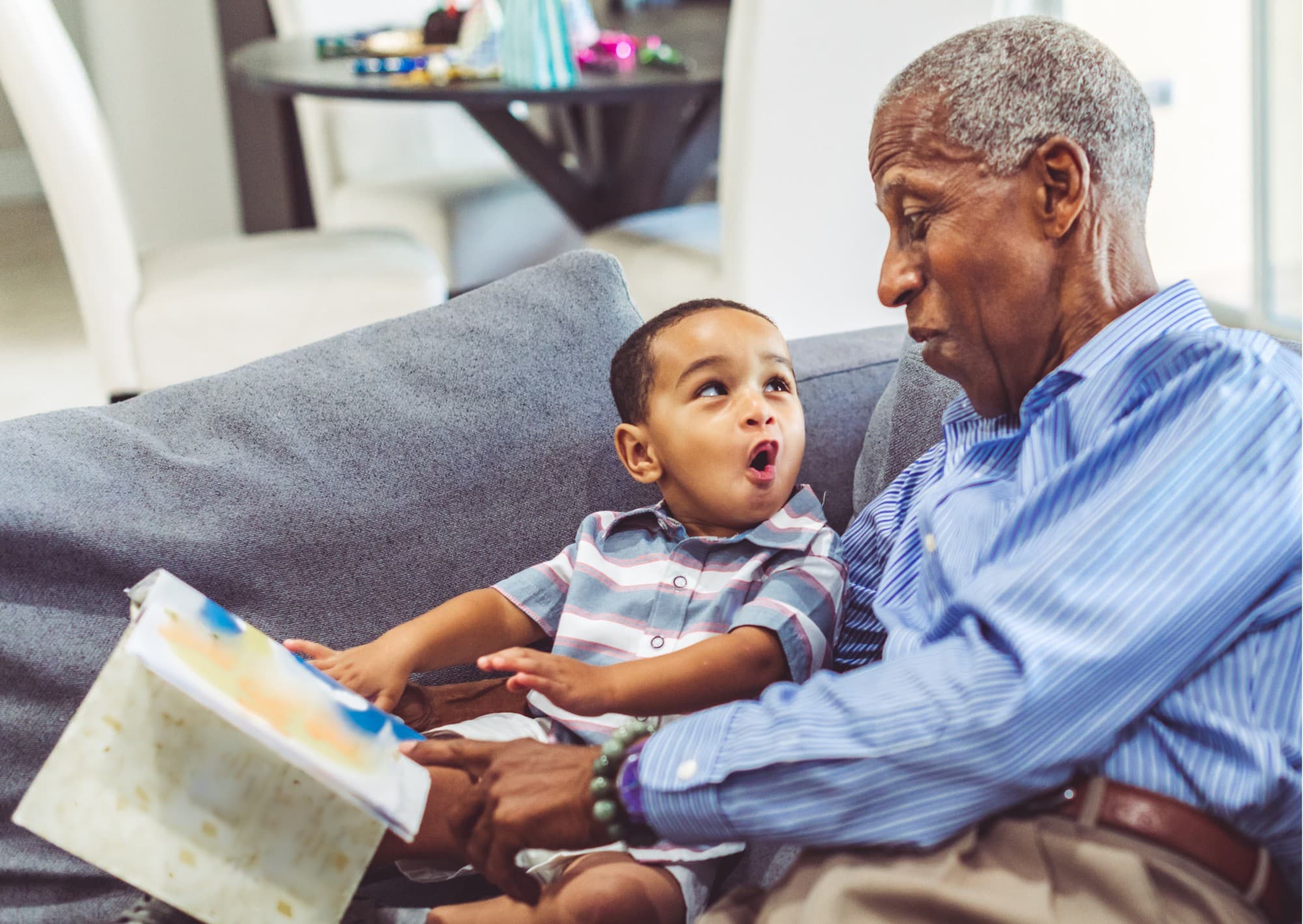 A grandfather reading a picture book with his grandson on the couch