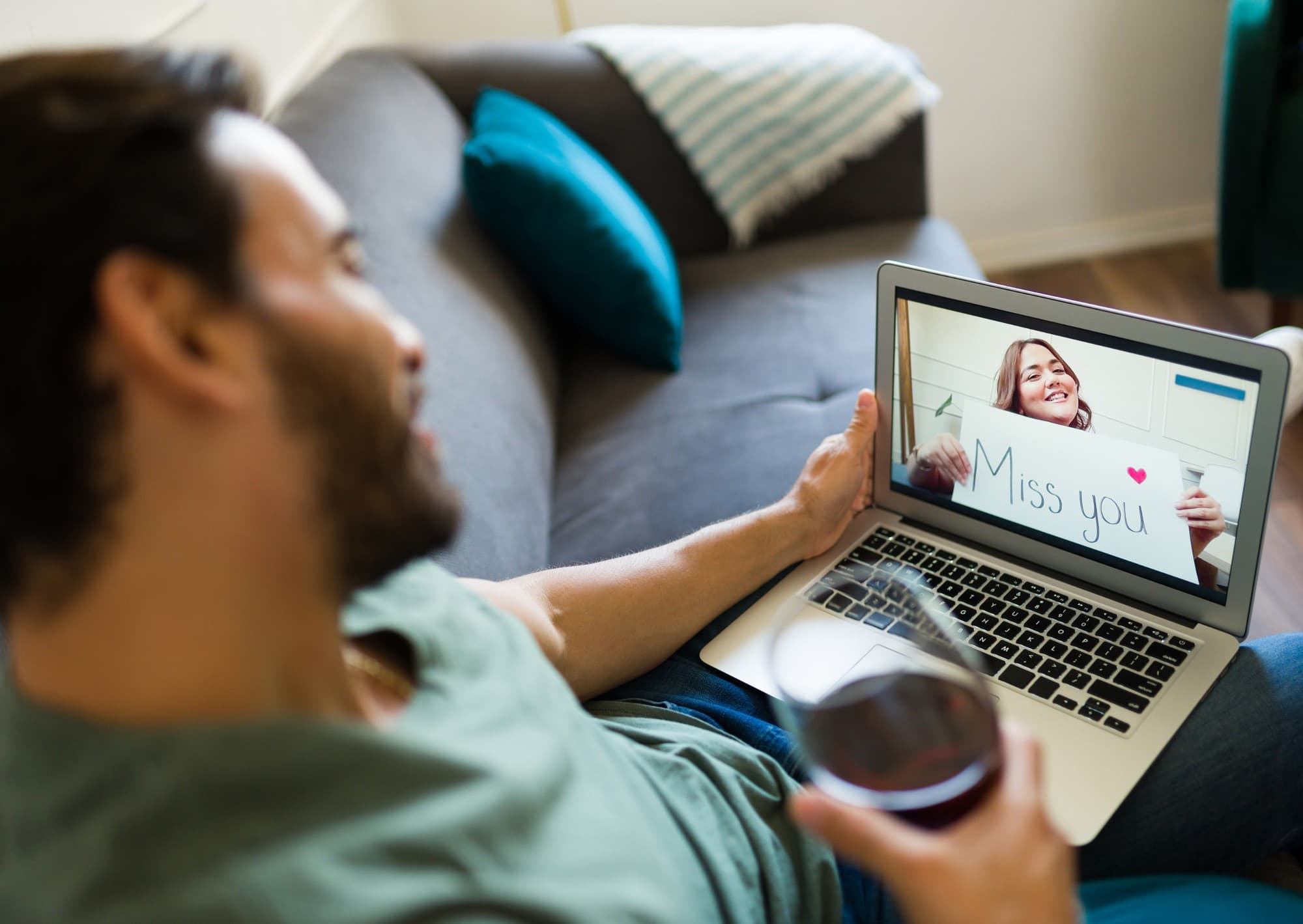 A man on a couch video-calling a woman holding up a "Miss you" sign